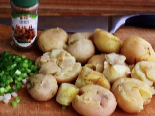 烧烤风味的香煎孜然小土豆,把蒸熟的红皮小土豆趁热去皮后，用刀的刀背轻轻压一下，这样做的目的是便于土豆在煎制过程中更好的入味，再把小香葱摘干净后清洗干净后，用刀切成小葱花，准备好烧开调料；