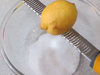 法式小甜点【椰蓉柠檬小方】,制做柠檬酱。将砂糖放入碗中,擦入2 个柠檬皮屑