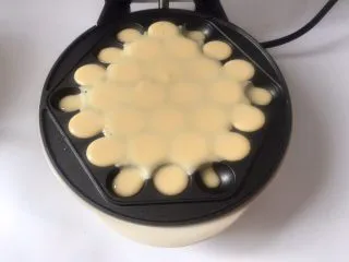 香港名小吃鸡蛋仔,倒入适量面糊,中间厚一点,边上少一点,免得溢出来,盖上盖子,戴上防烫手套将机器翻面倒立1分钟左右再翻回正面