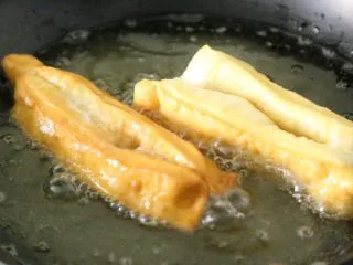 武汉小吃 糯米包油条,油锅烧热,将造型好的油条放入油锅浸炸,直至油条蓬松成金黄色,捞出沥干油备用。