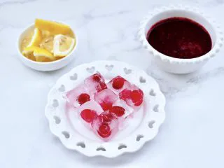 蔓越莓桑葚气泡水,把柠檬洗净后用刀切成片,榨好的蔓越莓桑葚汁盛到碗里,把冷冻好的冰块取出脱模。