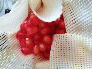 石榴气泡鸡尾酒,留出10余颗石榴粒,将其他石榴粒包入容器上的屉布里,用手用力挤压