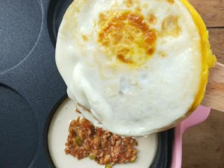 复刻街头美食~网厨第一个肉蛋堡,把步骤14的蛋饼取出翻面扣在这个新面糊肉馅上。 ~也就是鸡蛋这一面朝着刚刚做的面糊肉馅。
