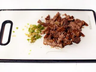 陕西小吃—肉夹馍,将酱好的牛肉切小块,将配菜青椒、青蒜切小丁混合后倒入一些酱牛肉的汤搅匀馅料。