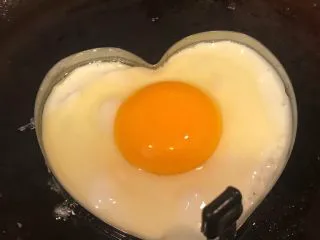 手抓饼开心早餐,锅中倒入适量底油加热摆入心形模具打入鸡蛋