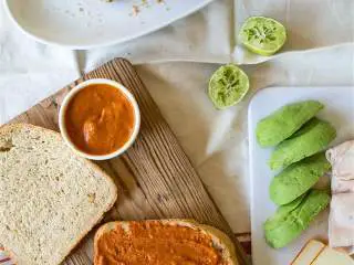 土耳其风味牛油果帕尼尼,用中低火预热煎盘，在法式面包 上抹做好的红辣椒酱，放上牛油果片，三明治火鸡肉 和门斯特芝士