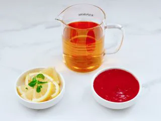 蔓越莓草莓花茶饮,把柠檬洗净后用刀切成片,榨好的蔓越莓草莓泥盛到碗里。