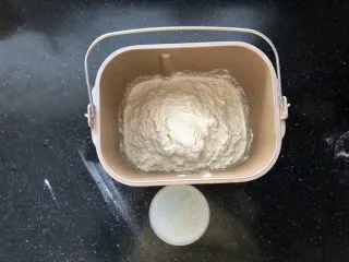 河南小吃-羊肉烩面,7、接下来制作烩面的面胚。把食用碱和盐倒入温水中融化,面粉放入面包机中。