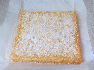 法式小甜点【椰蓉柠檬小方】,将烤好的柠檬方块在模具中略微放凉后取出,表面撒上一层椰蓉