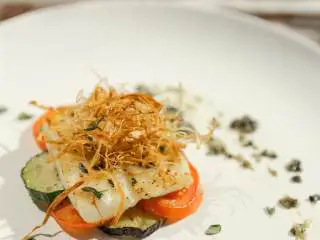 南法风味香煎银鳕鱼,装盘: 在蔬果上摆上鱼和京葱,鱼皮朝上,周围摆橄榄酱,淋上少许橄榄油,最后撒上罗勒叶碎。