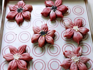 中式甜点～蜜豆桃花酥,依次做好所有的桃花的形状，放在垫油纸的烤盘中，再每个桃花酥中间抹上蛋液。再撒上给白芝麻，如图。