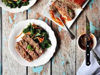 经典肉饼配羽衣甘蓝,肉饼烤好后,从烤箱中取出,拎起烘焙纸边缘脱模,放在盘子上。