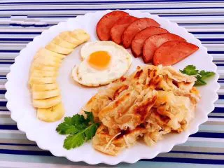 手抓饼开心早餐,煎好的手抓饼、鸡蛋、火腿还有切好的香蕉摆入盘中