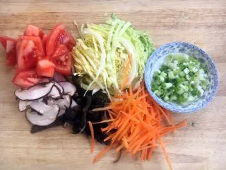 天津特色小吃 蔬菜烩饼,将圆白菜切丝,胡萝卜切丝,木耳切丝,香菇切丝,西红柿切块,小香葱切成葱花。