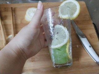 青提柠檬气泡水—夏天的快乐,准备一个玻璃杯，先放青提，用筷子或者其他工具把青提碾碎，柠檬贴在杯壁上