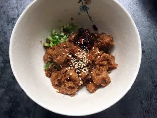 四川乐山名小吃—粉蒸肉卡饼,取适量粉蒸肉放入香菜小葱碗中,加入适量油辣椒,芝麻拌匀。
