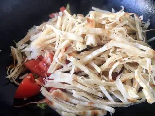 天津特色小吃 蔬菜烩饼,再放入大饼丝,盖上锅盖儿,中火,焖1分钟。锅底的蔬菜散出的热气将大饼丝焖软。