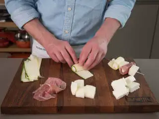 地中海风味菲达芝士烤串,取半份菲达块，每块分别卷入一条西葫芦片中。剩下的半份菲达块则卷入熏火腿片中。