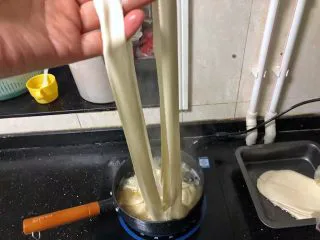 河南小吃-羊肉烩面,17、把面胚抻长后从中间的压痕一分为二,放入锅中。