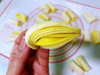姜黄花卷，饮料做,拿一半起来，两手各捏一头，扭一下，左手朝内扭右手朝外扭，将两头收到底部捏好，纹路漂亮的花卷就成型了。