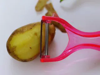 家常辣炒土豆丝,土豆洗净后,用削皮刀去除土豆外皮。