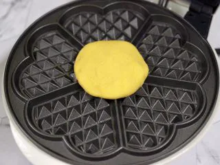 南瓜酸奶华夫饼,华夫饼机提前预热后，刷上薄薄的一层黄油，把摁扁的面饼放入机器里，盖上盖子开始烙制。