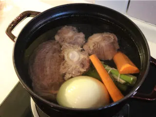 法式牛肉暖锅,将飞完水的牛腱子、牛尾,还有煮汤用的胡萝卜、大葱叶子、洋葱、香料包一起放入锅中,煮沸后小火慢炖2-3小时。
