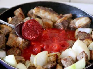 #食二星座#法式红酒炖牛肉 Boeuf Bourguignon,7.将肉拔到边上，倒入罐装番茄碎100克，舀勺番茄膏30克拌炒，并加少量的糖综合酸味。 注：没有罐装番茄碎和番茄膏就用2-3个大西红柿代替，一定要炒，炒了才香，并且可去除酸味。