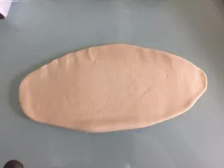 德国碱水面包普雷结,取1个面团擀成椭圆形,卷起来捏紧收口