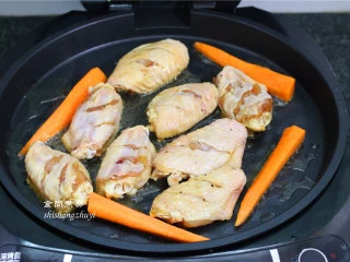 九层塔烤鸡翅,煎烤机接通电源,预热片刻,倒入食用油,将腌制过的鸡中翅和胡萝卜放入煎盘内