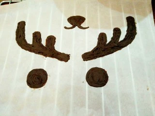 麋鹿奶油蛋糕,黑巧克力装进裱花袋，隔热水融化（大概50℃左右，不可以用开水） 事先在油纸上画出需要的麋鹿角，眼睛和鼻子 再用巧克力描出来，最好厚一点，太薄容易断定型备用