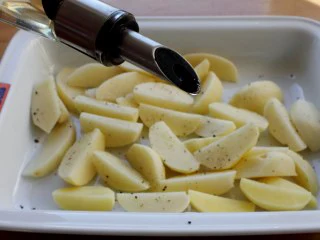 苹果柠香烤鸡腿,将土豆放入烤盘里，撒点胡椒、盐，浇点油拌匀。 