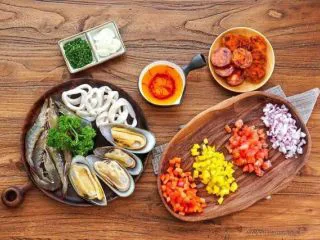 西班牙海鲜饭,大蒜切片，洋葱甜椒切丁，番茄去皮切丁，欧芹切碎。青口刷洗干净，鱿鱼去内脏软肋清洗干净切圈，大虾去虾线，腊肠切片。