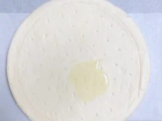 蜜瓜蔬果披萨,披萨饼底抹上一层油,将油底面朝下,放在油纸烤盘上。