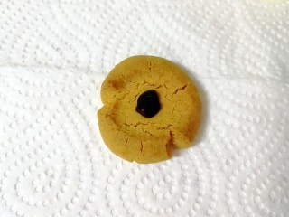 万圣节蜘蛛饼干,巧克力装进裱花袋隔水化开，剪开一个小小的口，取一个晾凉的饼干，挤上巧克力。