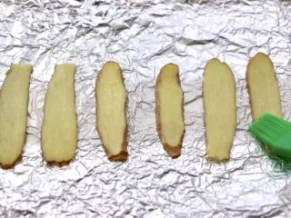 香辣孜然烤鱼,烤盘上铺上锡纸，放入姜片，这是为了在烤鱼的时候，不让鱼皮脱落掉，软化后的黄油，用刷子蘸少许把姜片刷一层薄薄的黄油。