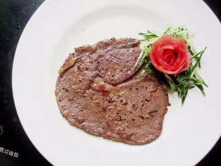 黑胡椒牛排，自制简单西餐,把煎好的牛排移动到盘子里，擦一些黄瓜丝放在旁边，摆上之前做好的西红柿花当做装饰
