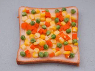 田园时蔬吐司披萨,把焯过水的玉米粒和豌豆，胡萝卜丁均匀地铺上奶酪片上。