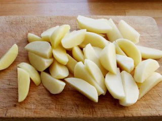 苹果柠香烤鸡腿,将土豆削皮、切成船形。 