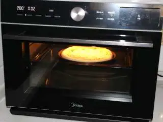 自制培根披萨,烤箱200度提前预热,预热好后将披萨饼底放入烤箱中层,烤3分钟。