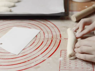 绵绵脆巧奶油包,将擀好的面片翻一面,转90度,从上往下卷起,形成长条形。 为什么要翻一面,因为刚才擀椭圆的时候光滑的一面是在上面,底下是有气孔的粗糙面,面团整形要注意让光滑面朝外,面团表面一直保持光滑收紧的状态。