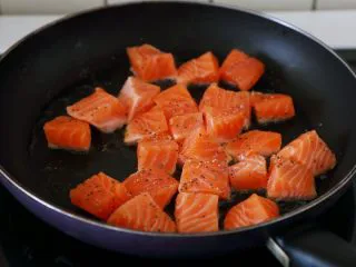 双椒土豆三文鱼,锅里多倒些油，油热将三文鱼块下锅，撒些黑胡椒碎和盐。