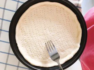 芝士培根披萨,将面饼装入烤盘,面饼四周略高于底部翘起,用叉子在面饼底部戳一些小点,以防烤制时底部膨起。