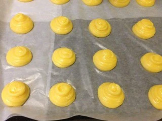 芋泥肉松泡芙,不要太拥挤,尽量保证大小高度一致,上下左右留出3cm左右的空隙以便烤的过程中膨胀。 挤完以后用手沾水将泡芙顶上的小尖儿按扁,避免在烘烤时上色太快烤焦。