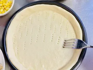 一次发酵——虾仁牛肉肠披萨,发酵好的饼皮取出，用叉子扎一些小洞，防止饼皮烘烤时鼓起。