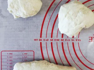 当主食一次可以吃三个的法棍面包,发酵至两倍大小,取出面团排气,分成三等份,依次擀成长舌状,卷起来。