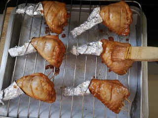 奥尔良鸡翅包饭,预热烤箱180度10分钟，饭都塞好后，用牙签封住口，不让米饭露出，再用锡纸包住翅尖，这样不会烤糊，刷上腌料+油。