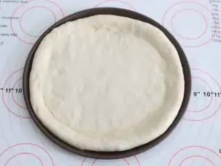 自制培根披萨,用擀面杖将面团擀成一个与披萨盘盘底一样大小的饼底,把饼皮铺进去。