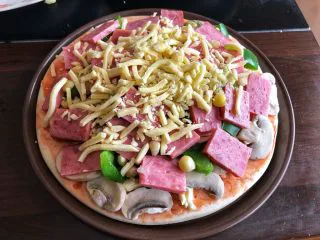 蔬菜火腿披萨,摆上口蘑，青椒，火腿和玉米粒，在上面再铺一层芝士。