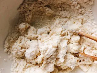 芝士培根披萨,多次少量加温水,用筷子搅拌成如图所示面块,底部还有少许面粉状态。(用温水揉面更易发酵)
